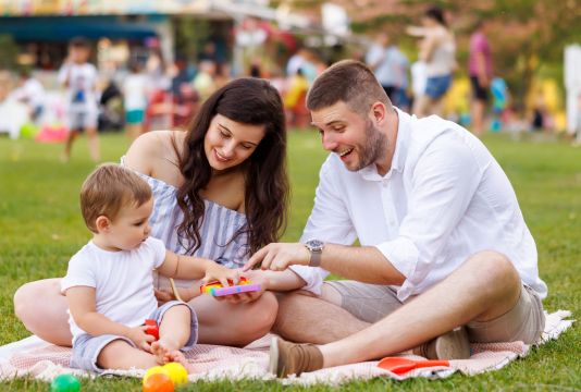 Zwei junge Eltern beim Picknick und spielen im Park